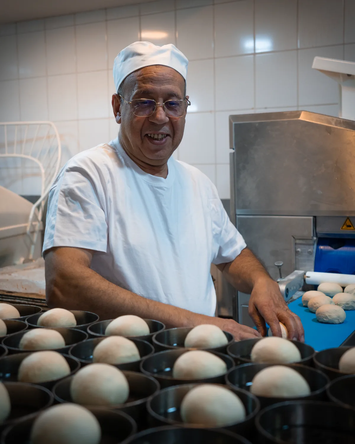 Jamal Ahlaloum souriant au fournil, devant des moules garnis de pâtons de pain burger